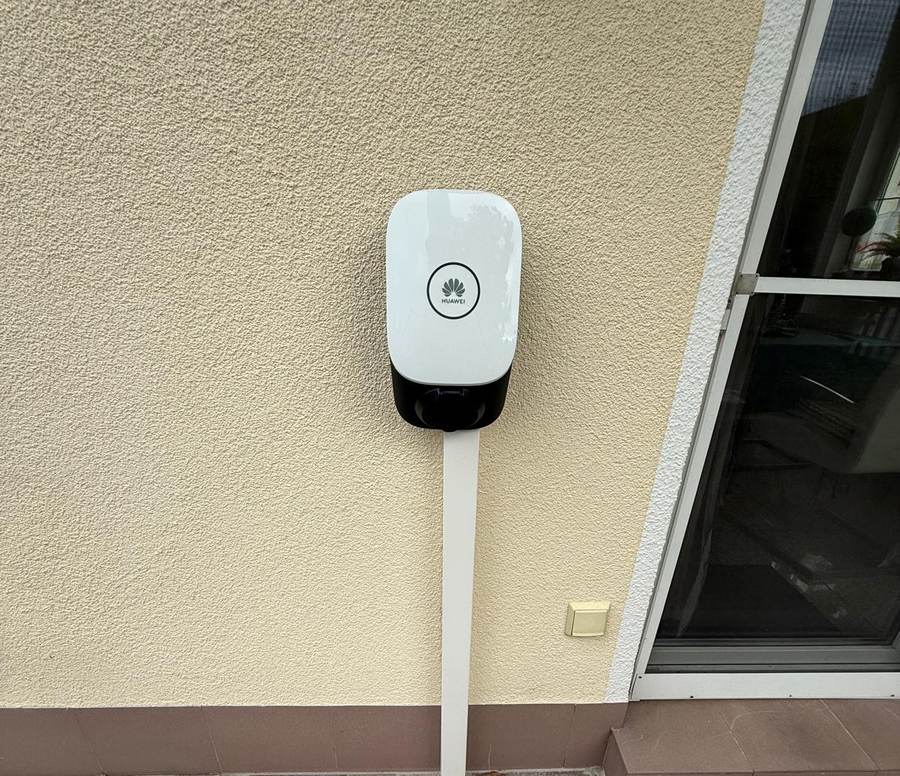 Fertig montierte weiße Wallbox an einer Hauswand, die Zuleitung läuft in einem sauber gesetzten weißen Kabelkanal senkrecht nach unten